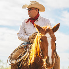 Man in cowboy hat and scarf riding a horse with a clear sky background
