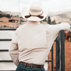 Person wearing a cowboy hat and light-colored shirt, standing in an outdoor setting with horses.